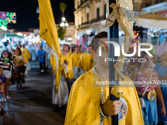 A member of the confraternity is participating in the procession of the statue of the Three Saints of Bisceglie among the stalls set up for...