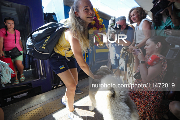 Ukrainian sabre fencer Yuliia Bakastova, who is winning gold in the Women's Sabre Team Gold Medal Match, is petting a dog on the platform of...