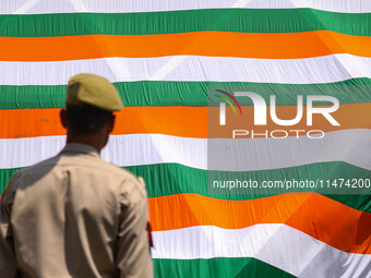 An Indian Policeman is looking at the Indoor stadium building with a giant Indian tri-color ahead of India's Independence Day celebrations i...