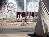 Displaced Palestinians are walking near their tents at a makeshift displacement camp set up on a roadside in Deir el-Balah in the central Ga...