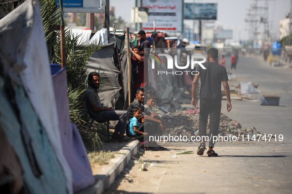 Displaced Palestinians are sitting by their tents at a makeshift displacement camp set up on a roadside in Deir el-Balah in the central Gaza...