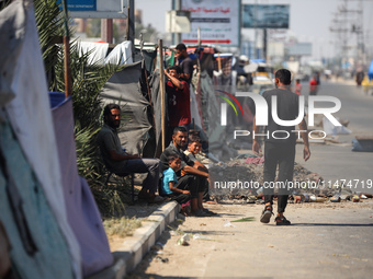 Displaced Palestinians are sitting by their tents at a makeshift displacement camp set up on a roadside in Deir el-Balah in the central Gaza...