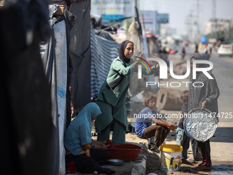 A Palestinian girl is carrying water at a makeshift displacement camp set up on a roadside in Deir el-Balah in the central Gaza Strip on Aug...