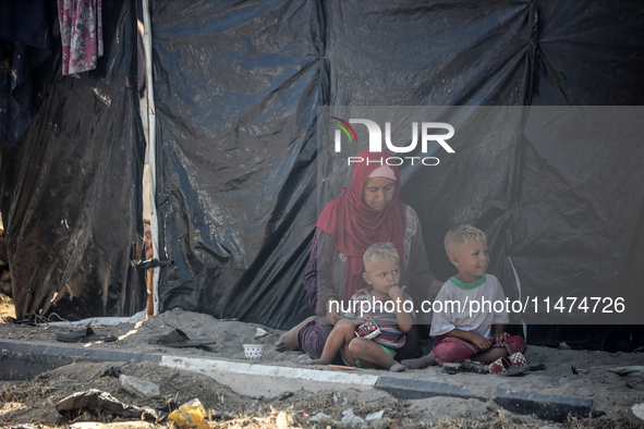 Displaced Palestinians are sitting by their tents at a makeshift displacement camp set up on a roadside in Deir el-Balah in the central Gaza...