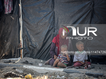 Displaced Palestinians are sitting by their tents at a makeshift displacement camp set up on a roadside in Deir el-Balah in the central Gaza...