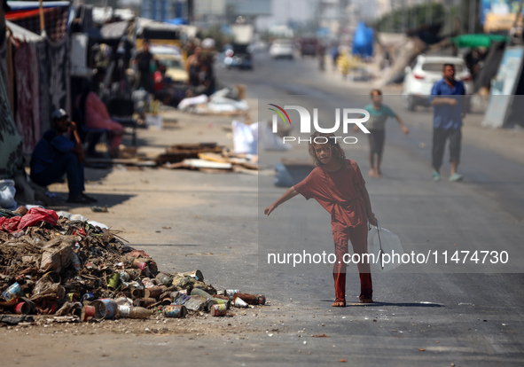 A Palestinian girl is carrying water at a makeshift displacement camp set up on a roadside in Deir el-Balah in the central Gaza Strip on Aug...