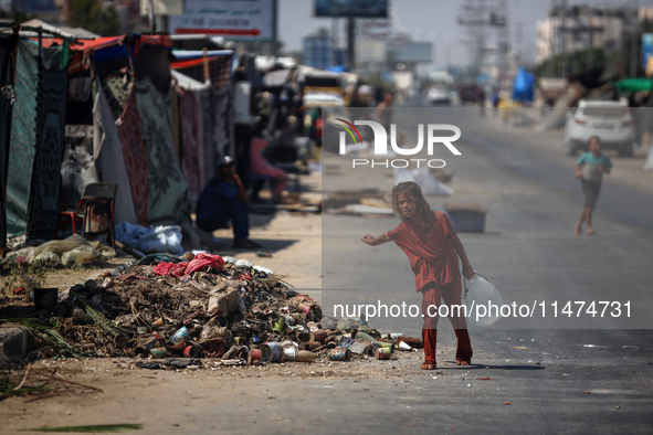 A Palestinian girl is carrying water at a makeshift displacement camp set up on a roadside in Deir el-Balah in the central Gaza Strip on Aug...