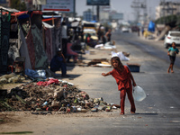 A Palestinian girl is carrying water at a makeshift displacement camp set up on a roadside in Deir el-Balah in the central Gaza Strip on Aug...