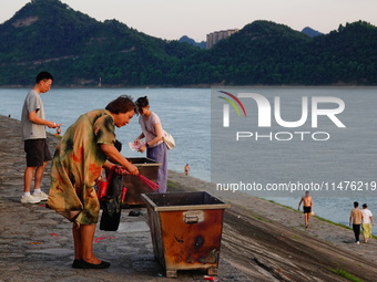 People are burning paper money to offer sacrifices to their ancestors at the Zhongyuan Festival near the banks of the Yangtze River in Yicha...