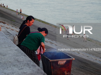 People are burning paper money to offer sacrifices to their ancestors at the Zhongyuan Festival near the banks of the Yangtze River in Yicha...