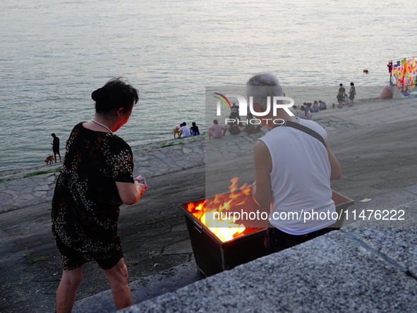 People are burning paper money to offer sacrifices to their ancestors at the Zhongyuan Festival near the banks of the Yangtze River in Yicha...