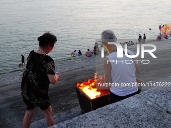 People are burning paper money to offer sacrifices to their ancestors at the Zhongyuan Festival near the banks of the Yangtze River in Yicha...