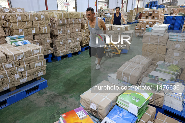 A staff member is carrying and arranging textbooks for the new semester at the textbook distribution center of New China Book Store in Zaozh...