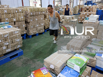 A staff member is carrying and arranging textbooks for the new semester at the textbook distribution center of New China Book Store in Zaozh...