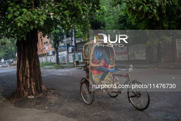 A rickshaw puller is tapping his phone while resting in his rickshaw in Dhaka, Bangladesh, on August 13, 2024. 