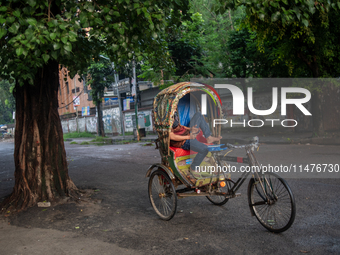 A rickshaw puller is tapping his phone while resting in his rickshaw in Dhaka, Bangladesh, on August 13, 2024. (