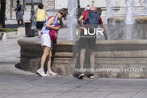 Tourist, visitors and locals are walking past Syntagma Square with the famous fountain during a heatwave in Athens with the high temperature...