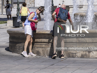 Tourist, visitors and locals are walking past Syntagma Square with the famous fountain during a heatwave in Athens with the high temperature...