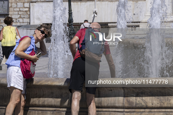 Tourist, visitors and locals are walking past Syntagma Square with the famous fountain during a heatwave in Athens with the high temperature...