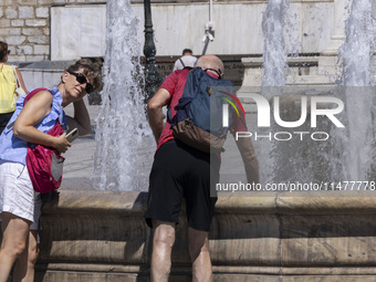 Tourist, visitors and locals are walking past Syntagma Square with the famous fountain during a heatwave in Athens with the high temperature...