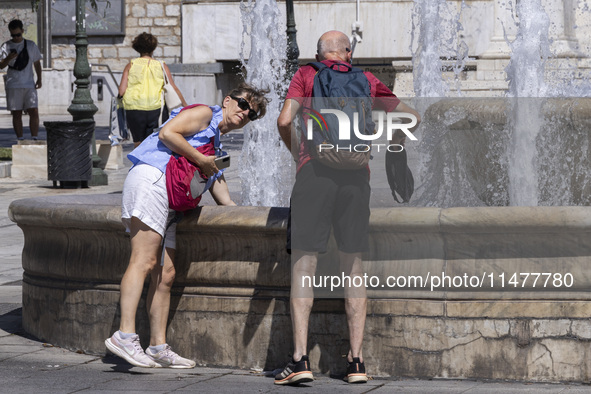 Tourist, visitors and locals are walking past Syntagma Square with the famous fountain during a heatwave in Athens with the high temperature...