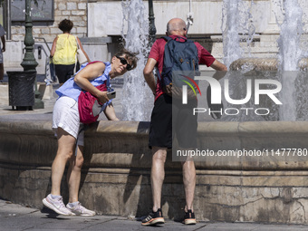 Tourist, visitors and locals are walking past Syntagma Square with the famous fountain during a heatwave in Athens with the high temperature...