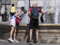 Tourist, visitors and locals are walking past Syntagma Square with the famous fountain during a heatwave in Athens with the high temperature...