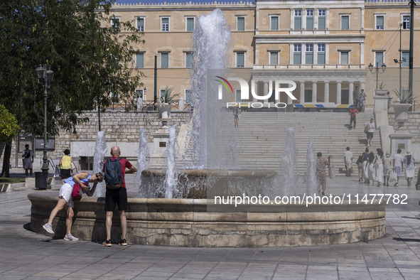 Tourist, visitors and locals are walking past Syntagma Square with the famous fountain during a heatwave in Athens with the high temperature...