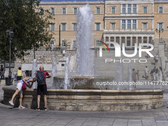 Tourist, visitors and locals are walking past Syntagma Square with the famous fountain during a heatwave in Athens with the high temperature...