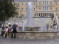 Tourist, visitors and locals are walking past Syntagma Square with the famous fountain during a heatwave in Athens with the high temperature...