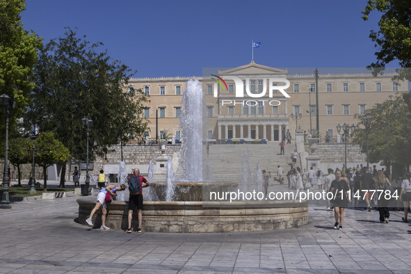 Tourist, visitors and locals are walking past Syntagma Square with the famous fountain during a heatwave in Athens with the high temperature...