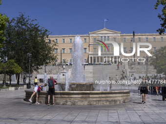 Tourist, visitors and locals are walking past Syntagma Square with the famous fountain during a heatwave in Athens with the high temperature...