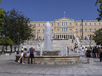 Tourist, visitors and locals are walking past Syntagma Square with the famous fountain during a heatwave in Athens with the high temperature...