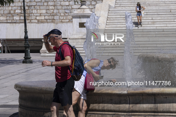 Tourist, visitors and locals are walking past Syntagma Square with the famous fountain during a heatwave in Athens with the high temperature...