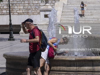 Tourist, visitors and locals are walking past Syntagma Square with the famous fountain during a heatwave in Athens with the high temperature...