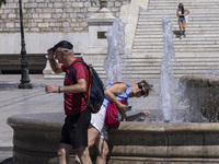 Tourist, visitors and locals are walking past Syntagma Square with the famous fountain during a heatwave in Athens with the high temperature...