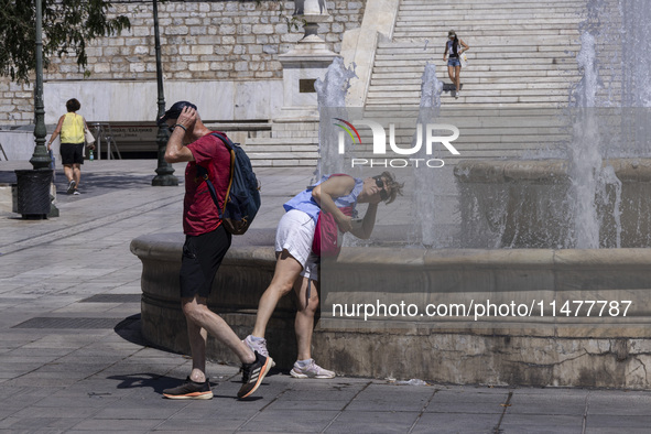 Tourist, visitors and locals are walking past Syntagma Square with the famous fountain during a heatwave in Athens with the high temperature...