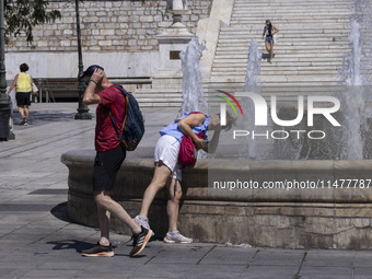 Tourist, visitors and locals are walking past Syntagma Square with the famous fountain during a heatwave in Athens with the high temperature...