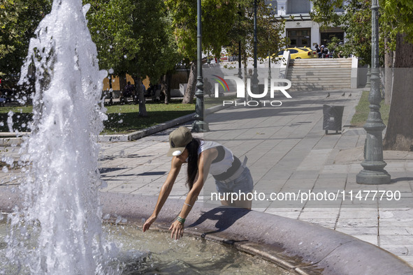 Tourist, visitors and locals are walking past Syntagma Square with the famous fountain during a heatwave in Athens with the high temperature...