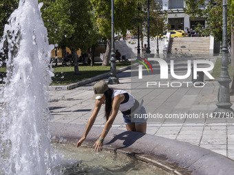 Tourist, visitors and locals are walking past Syntagma Square with the famous fountain during a heatwave in Athens with the high temperature...