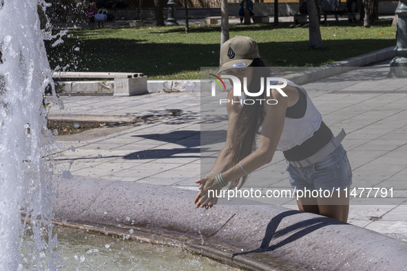 Tourist, visitors and locals are walking past Syntagma Square with the famous fountain during a heatwave in Athens with the high temperature...