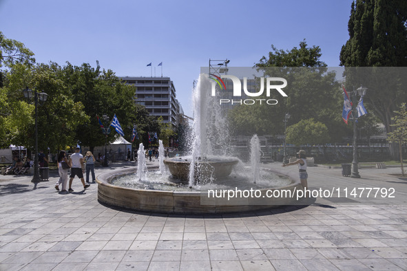 Tourist, visitors and locals are walking past Syntagma Square with the famous fountain during a heatwave in Athens with the high temperature...