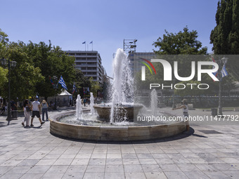 Tourist, visitors and locals are walking past Syntagma Square with the famous fountain during a heatwave in Athens with the high temperature...