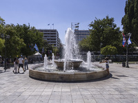 Tourist, visitors and locals are walking past Syntagma Square with the famous fountain during a heatwave in Athens with the high temperature...