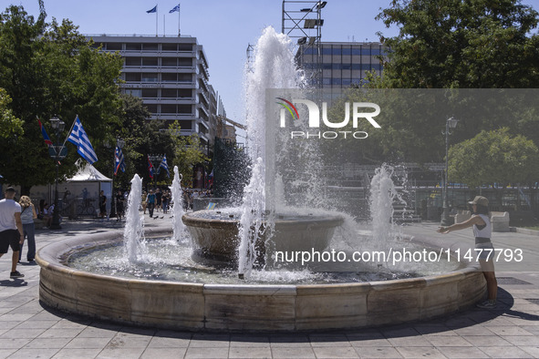 Tourist, visitors and locals are walking past Syntagma Square with the famous fountain during a heatwave in Athens with the high temperature...