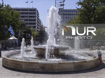 Tourist, visitors and locals are walking past Syntagma Square with the famous fountain during a heatwave in Athens with the high temperature...