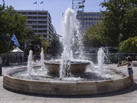 Tourist, visitors and locals are walking past Syntagma Square with the famous fountain during a heatwave in Athens with the high temperature...