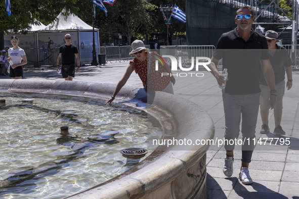 Tourist, visitors and locals are walking past Syntagma Square with the famous fountain during a heatwave in Athens with the high temperature...