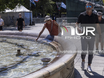 Tourist, visitors and locals are walking past Syntagma Square with the famous fountain during a heatwave in Athens with the high temperature...