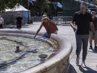 Tourist, visitors and locals are walking past Syntagma Square with the famous fountain during a heatwave in Athens with the high temperature...